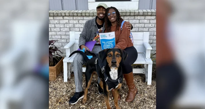 Couple poses with black and tan hound mix dog outside of shelter to celebrate adoption