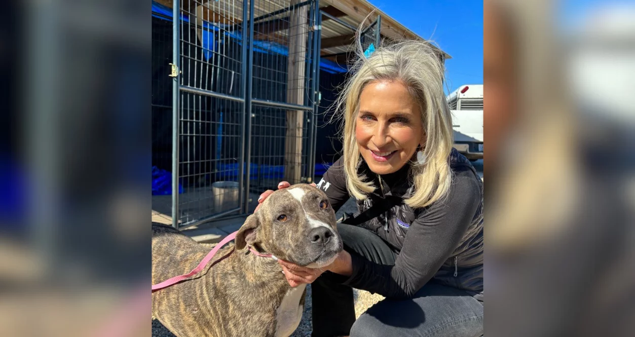 Cathy poses outside of kennels with brindle pitbull mix