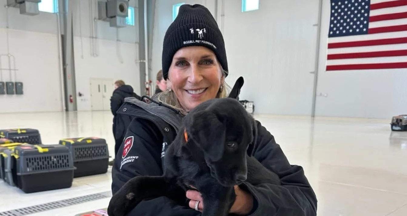 Cathy Bissell poses at a transport with a black lab puppy rescued from a puppy mill